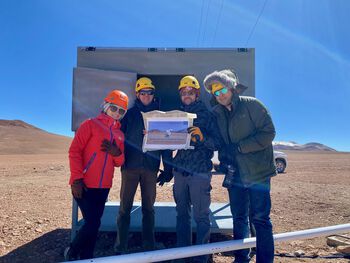 group photo of 4 people holding a poster on a desert landscape, blue sky, sunny day